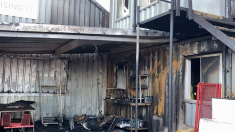 A fire damaged portacabin. The metal is burnt and there are items on the floor black from the smoke. 