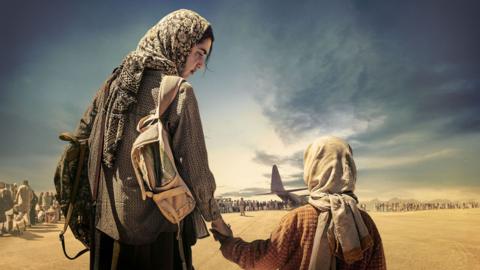 A woman holds a child's hand as they walk away from the camera. Both are wearing headscarves
