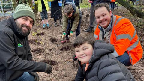 Three people smiling at the camera while planting shrubs on the banks of the dyke. 