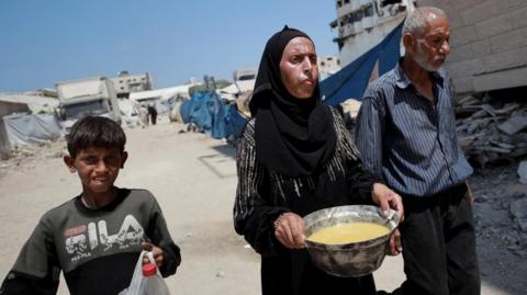 A Palestinian woman carries a bowl with food she received from a charity kitchen, amid a hunger crisis, in Gaza City, July 28, 2025