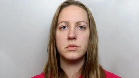 A custody photograph of Lucy Letby who has long blonde hair and and is wearing a red top.