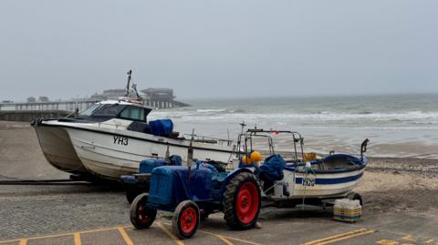 Small boats and tractors in front of a grey sea and grey sky