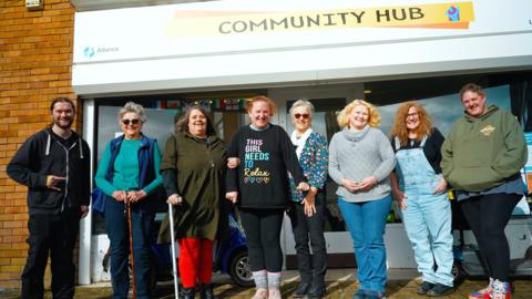 Members of the Serendipity Art and Craft Group standing side-by-side, pictured outside the community hub they use. 