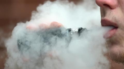 A man uses a vape and blows smoke out.
