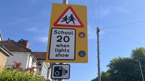 Sign that reads "School, 20 when lights show" and a speed camera signal. 