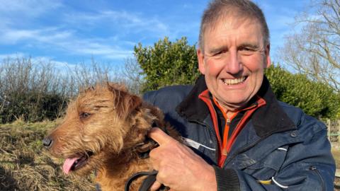 Branston the golden terrier dog and his owner David Benton who looks at the camera smiling.