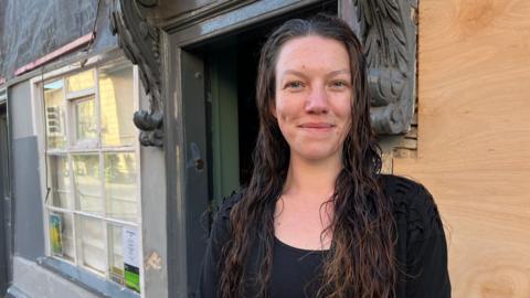 Jo Myers stands outside the pub smiling. She is wearing a black top and wears her brown hair long over her shoulders