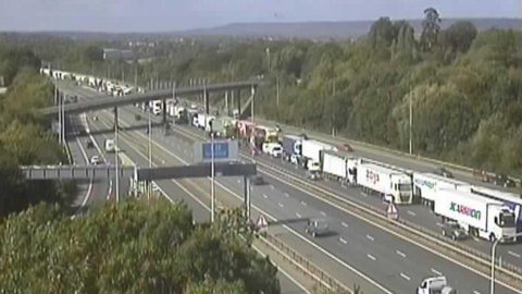 The M20 motorway from an aerial vantage point. One side is free-flowing and has few vehicles on it, while there is a long queue of traffic stretching into the distance on the other side.