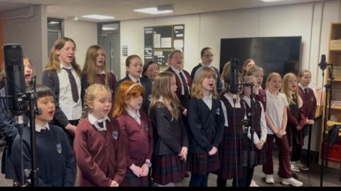 Clann-sgoile bho Bhun-sgoil Bhaile Ghobhainn a' seinn ann an còisir.