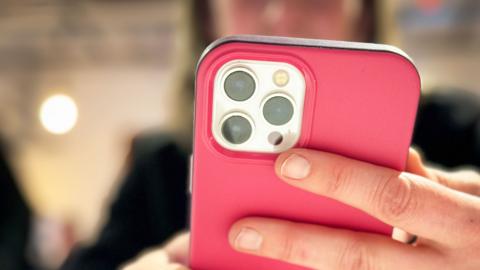 An out-of-focus woman looks at the screen of an iPhone in a pink cover