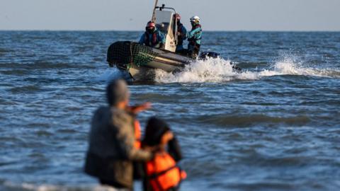 A French Navy boat sails past migrants trying to board a boat in an attempt to cross the English Channel 