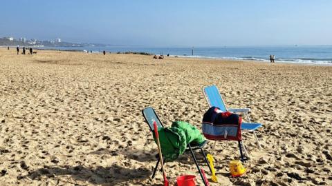 Two seats on a beach with buckets and spades on the ground and blue sky and sea behind