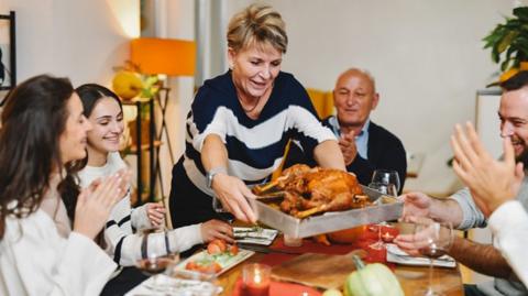 A woman serves up a roast to a family at a dining table