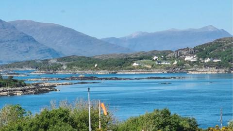 Blue sky over a loch with mountains in the distance 