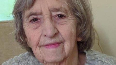 Emma Finch faces the camera, half-smiling. She has neck-length light-brown/grey hair and wears a light grey jumper.