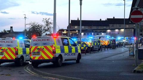 Multiple police vehicles under blue lights at the scene of what was described as a youth disorder incident.