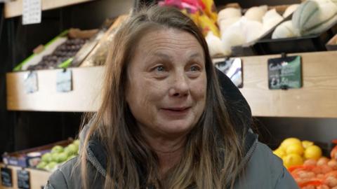 A woman in a shop with a brown coat and brown hair.