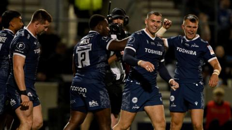 Nathan Jibulu (centre) holds his arm out to a team-mate in celebration of his try