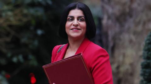 Shabana Mahmood wearing a bright pink jacket and carrying a file 