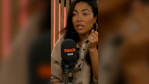 Emma Grede wearing a beige buttoned jumper. She is sat in front of a black microphone which has 'Radical' and 'BBC' on it.