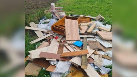 Fly-tipping dumped on field including lots of wood of different sizes and what looks like a barber's chair