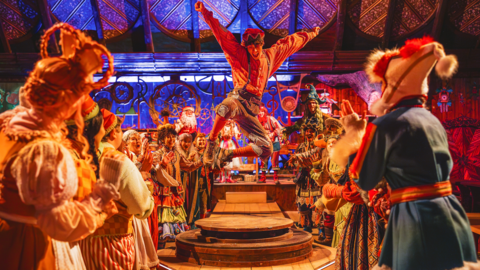 A man dressed as an elf dances on a wooden table surrounded by people dressed in festive costumes.