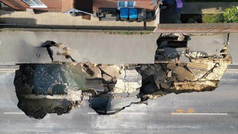 An aerial view of a 60ft sinkhole in a stretch of road with water in the bottom
