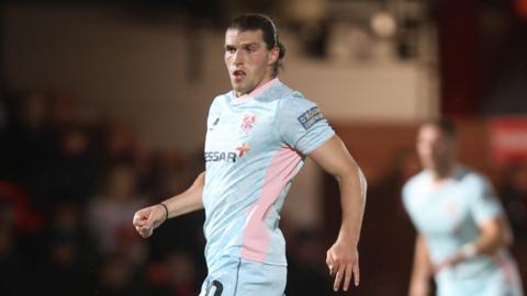 Josh Davison is match action for Tranmere wearing a white kit with a pink stripe down the sides of the shirt