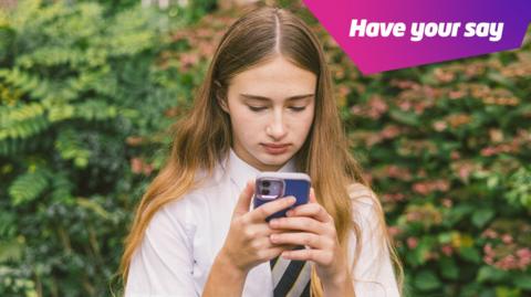 A girl in school uniform looks at her phone