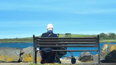 A person sitting on a bench, they have their back to the camera