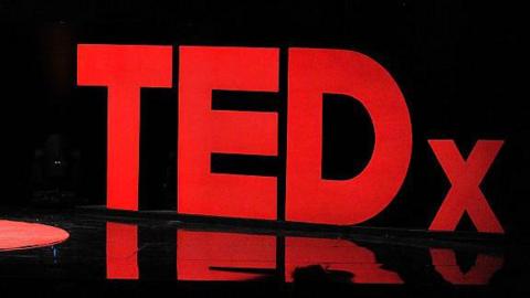 A TEDx red sign that sits on a stage during a talk. 