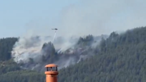 A helicopter in the distance drops water on the woodland and grass fire in Macclesfield Forest, smoke is visable.
