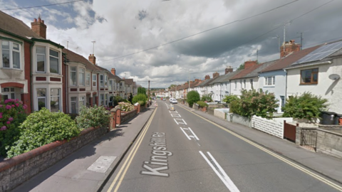 A Google Maps screenshot of the road, taken from uphill. It is a sunny day with some clouds, and the street is made up of lots of terraced houses.