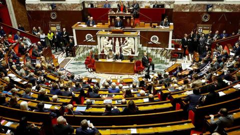 A wide shot of the interior of the French National Assembly in Paris, with Michel Barnier addressing politicians