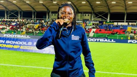 Nigerian football referee Gbemisola Yusuf poses on the pitch in a stadium and bites a medal between her teeth