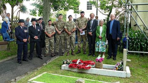 A group of people including four members of the military are standing by Sapper Onions' grave.