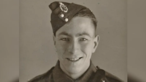 John Maskell is photographed during World War Two in his uniform. The photo is sepia coloured, Mr Maskell is smiling.