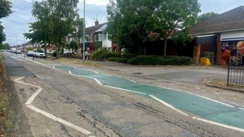 Section of Bricknell Avenue showing white and green road markings with houses and cars in background