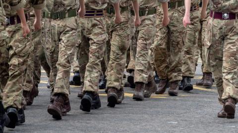 Close up shot of the legs of British soldiers who are in uniform and marching through the street
