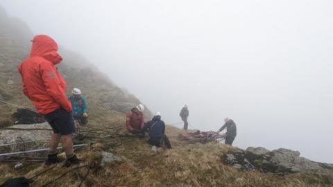 Rescuers prepare to lower a stretcher down the fell using ropes