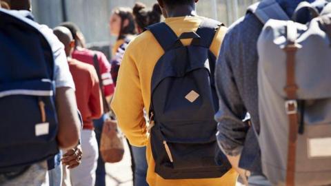 The backs of a group of students carrying backpacks. They are unidentifiable.