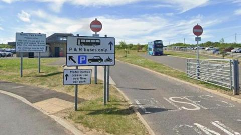 The entrance to the park and ride site. There is a sign indicating only park and ride buses may enter, with a different sign indicating where the public can park.