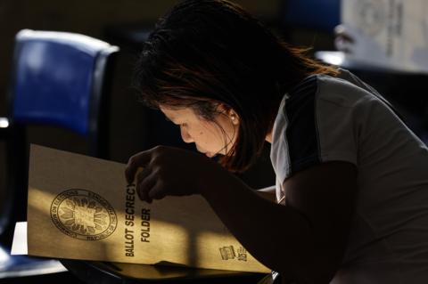 A woman looks inside a folder with the words 'BALLOT SECRECY FOLDER' written on the front