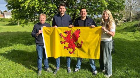 Four people stood holding a yellow flag featuring a red dragon.