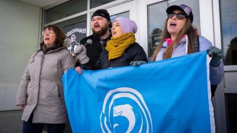 Daoine a' togail fianais le bratach Comhairle na Gàidhlig