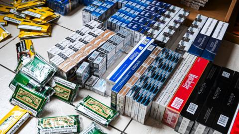 Numerous boxes of cigarettes and tobacco pouches scattered on the floor.