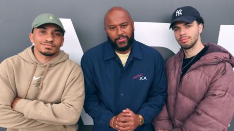 Richie Brave wearing a navy blue jacket alongside two men