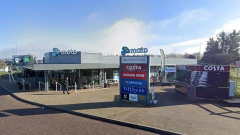 A wide view of Exeter Services on the M5 showing the entrance to the Moto building and a large sign advertising food and drink suppliers.