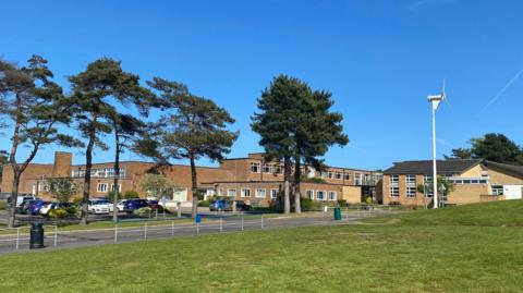 View of the school site at Sheringham. There are multiple brick buildings with trees surrounding them.