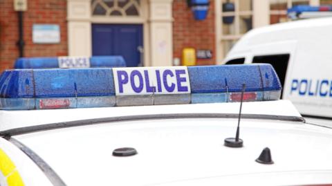 A stock image of a police officer's car. The top of the vehicle is visible with its blue lights.